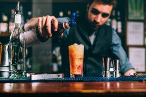 Portrait Of Bartender Pouring Cherry Syroup In Orange Summer Cocktail. Details Of Bar And Restaurant - Terceirização Financeira | Hands Financeiro